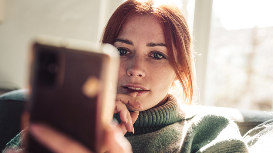 A young woman engaging with social media on her phone, emphasizing social media marketing strategies.